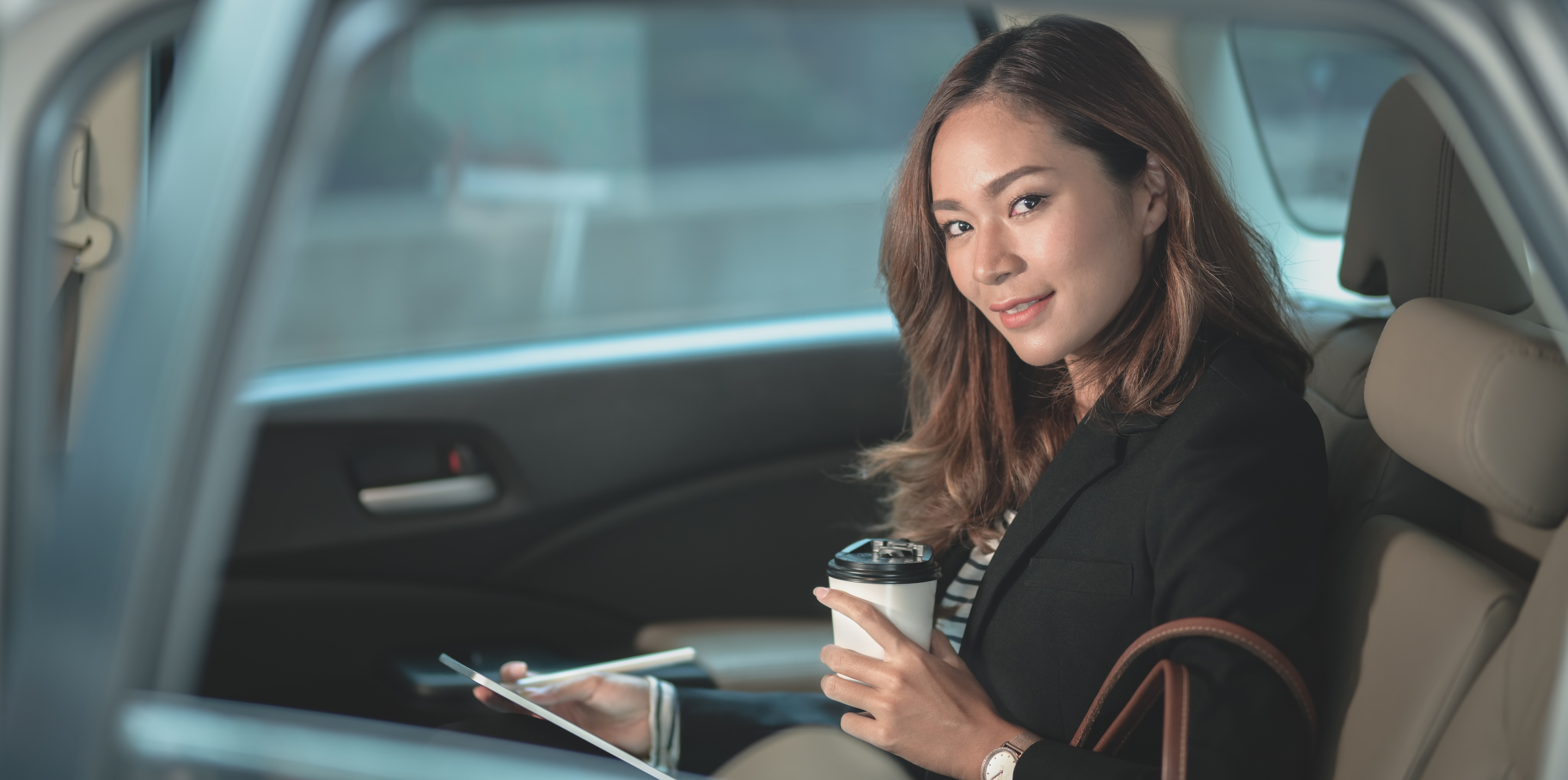 Asian woman sitting with tablet and coffee in car